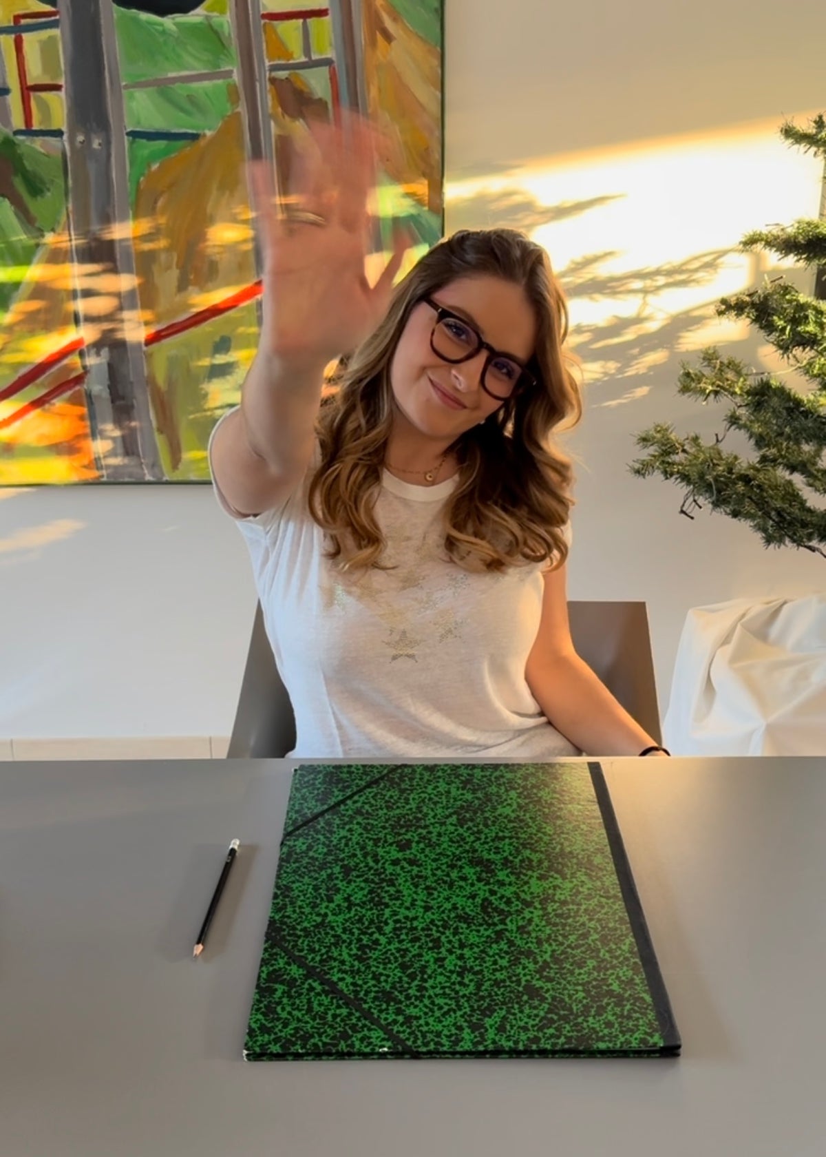 Rosana, créatrice de JUSTE, fait coucou à son bureau avec son carnet à dessin et son crayon